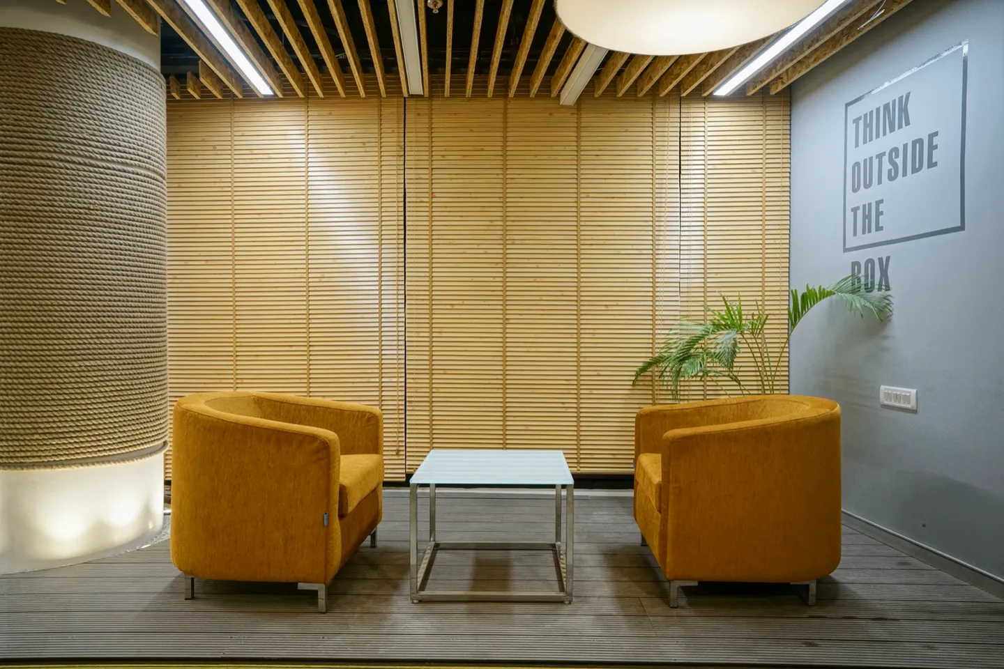 Mustard tub chairs and chrome side table against horizontal timber slat wall with rope-wrapped column — AIHP managed office, Gurgaon