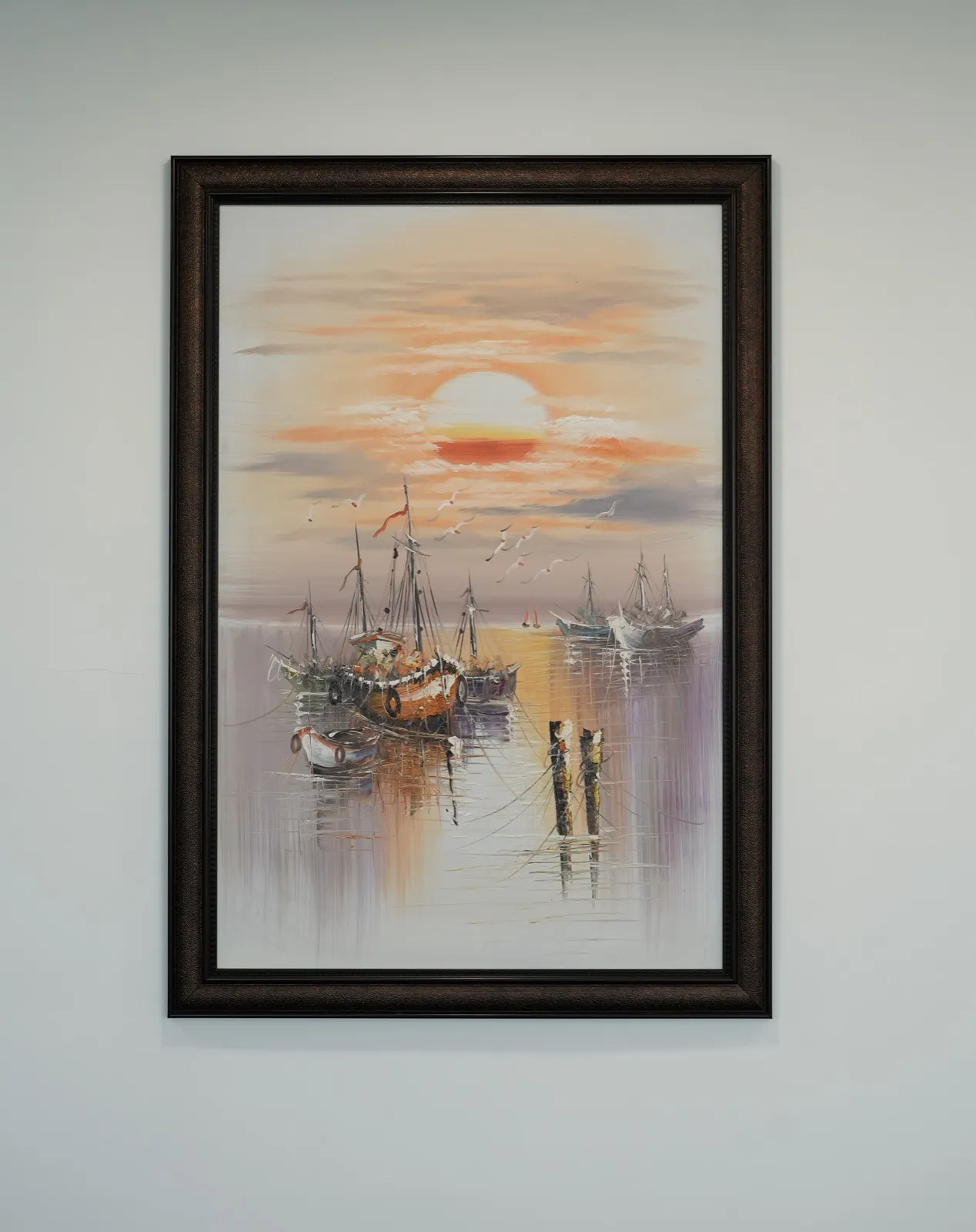 Framed sunset harbour oil painting in dark moulded frame on a pale grey wall — AIHP managed office, Gurgaon