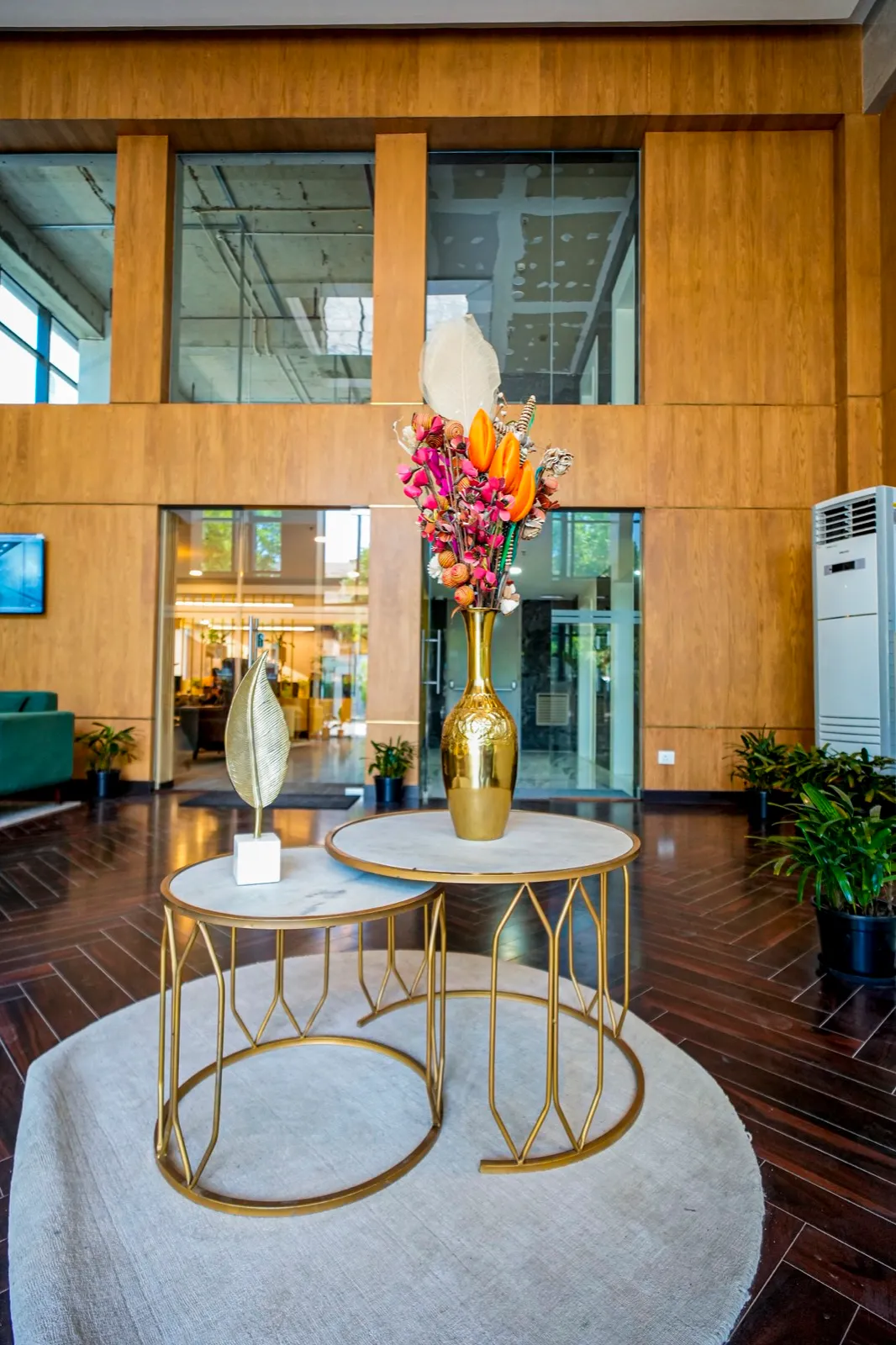 Round nesting tables with brass legs and gold vase of flowers in a double-height wood-panelled lobby — AIHP managed office, Gurgaon