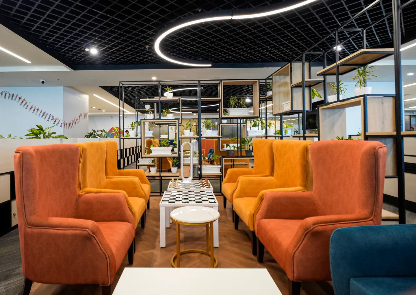 Orange and amber wingback booths around a chessboard table beside a black-grid planter divider — AIHP managed office, Gurgaon