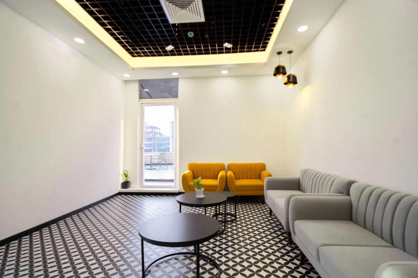 Grey sofa and twin mustard chairs with black round tables on monochrome patterned tile under coffered ceiling — AIHP managed office, Gurgaon
