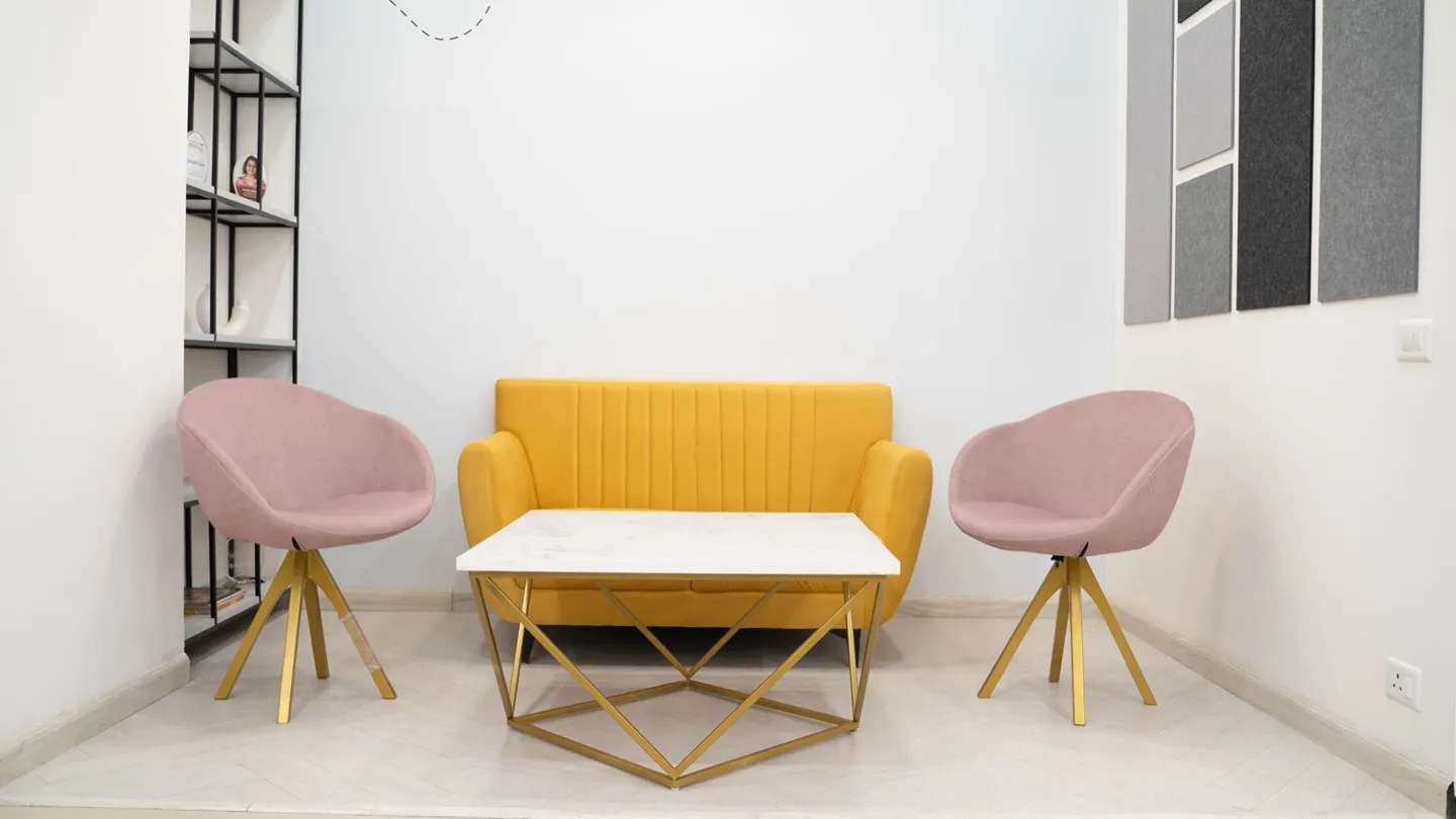 Maroon woven armchairs and white triangular-base tables by a slatted wood planter screen — AIHP managed office, Gurgaon