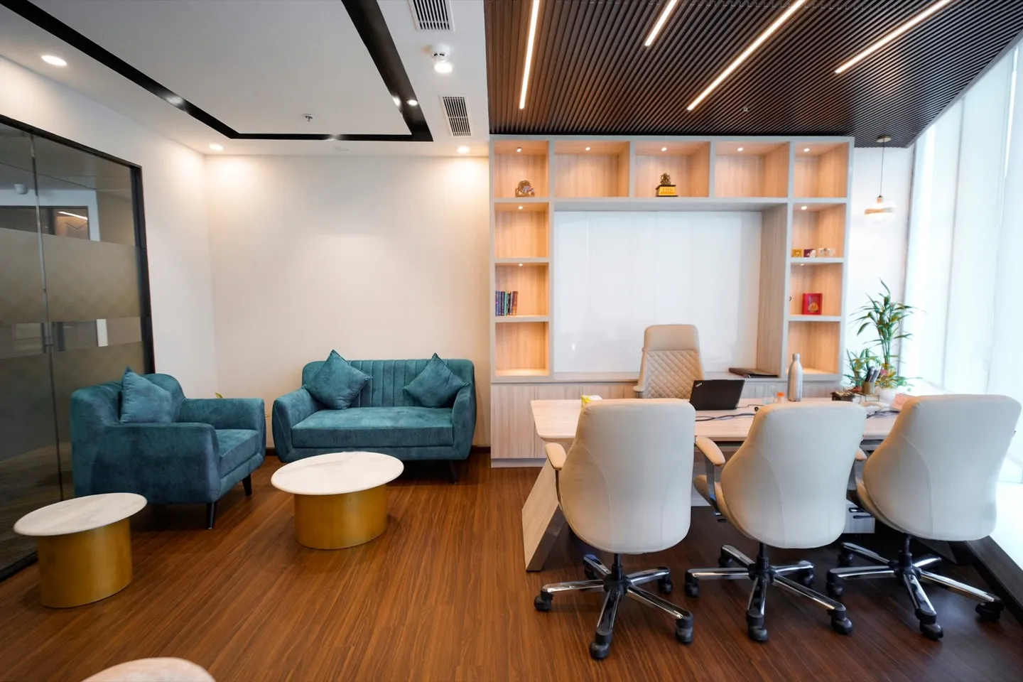Private cabin with teal sofa lounge, oak shelving wall and a desk with cream chairs on wood floor — AIHP managed office, Gurgaon
