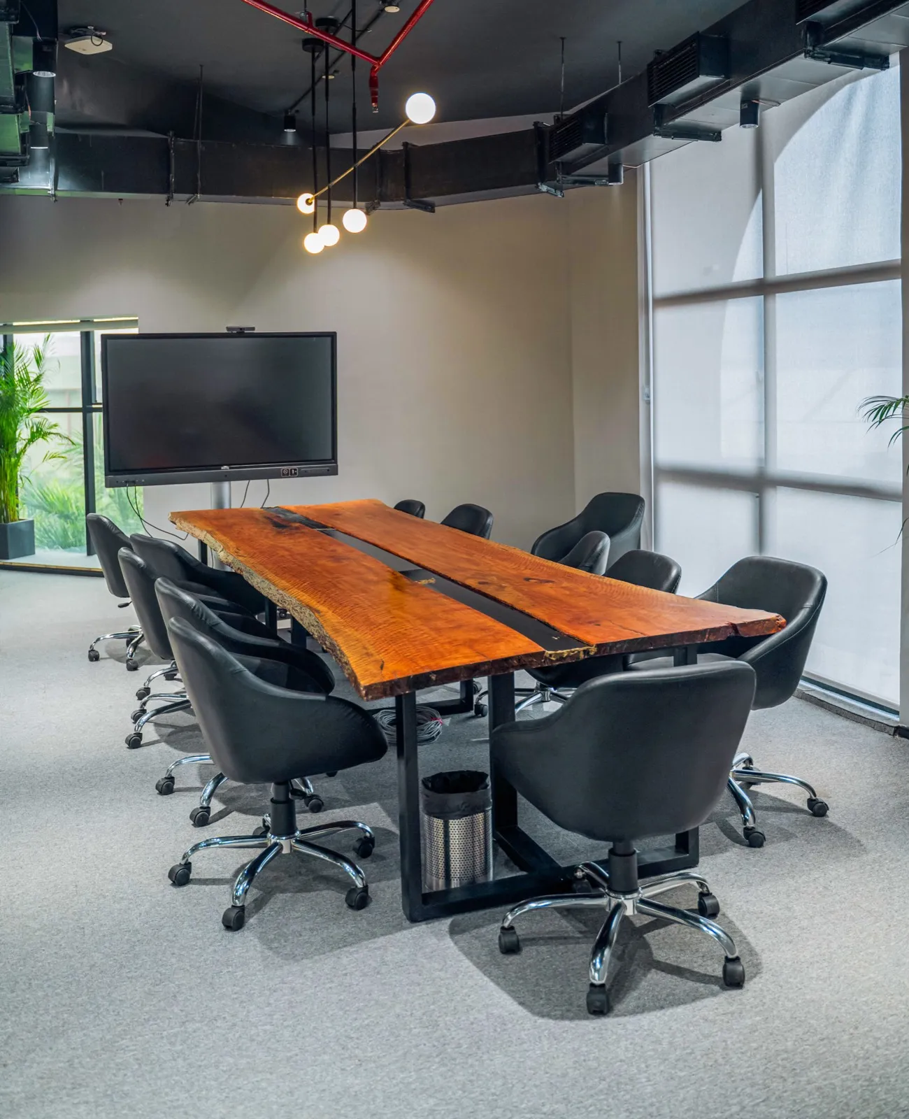 Ten-seat boardroom with a live-edge wood-slab table, black leather chairs and wall display — AIHP managed office, Gurgaon