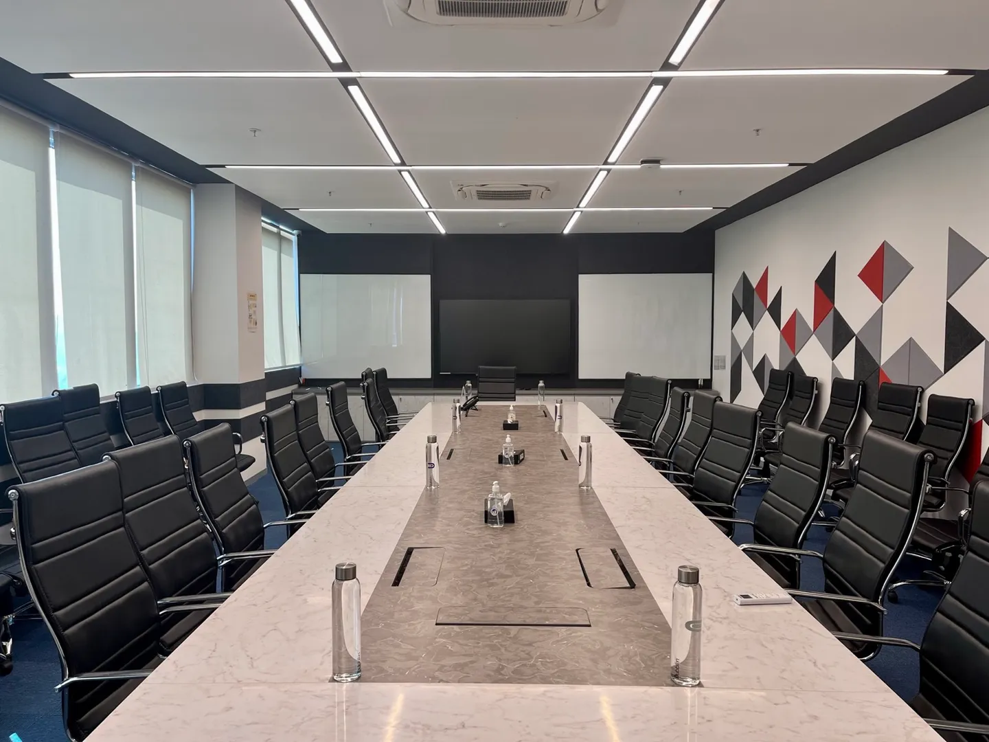 Long marble boardroom table for sixteen black chairs facing whiteboards and a diamond accent wall — AIHP managed office, Gurgaon