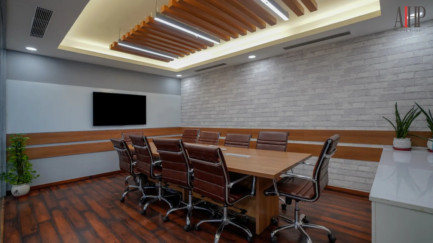Eight-seat room with wood table, brown leather chairs and wall TV under exposed brick — AIHP managed office, Gurgaon