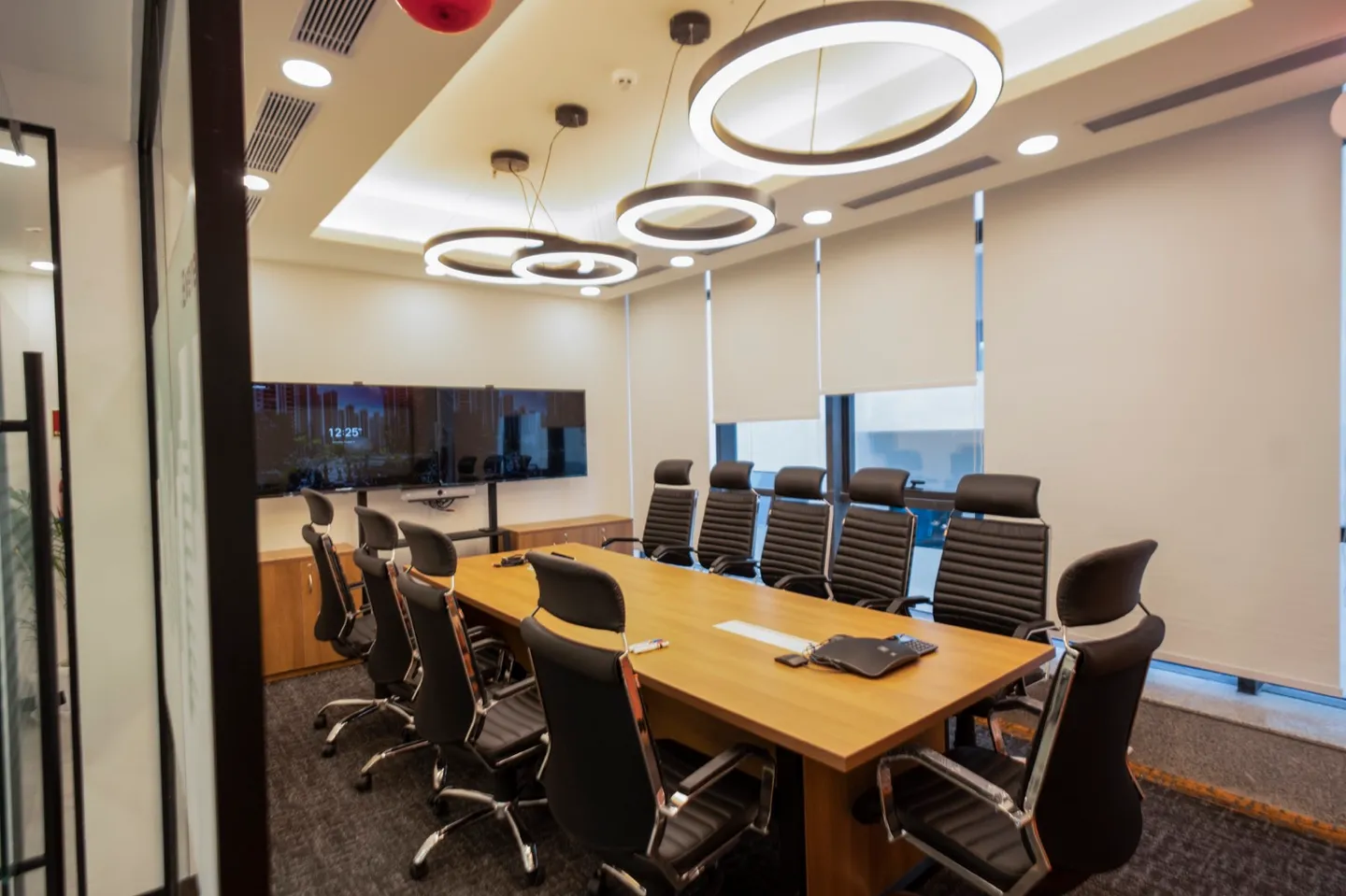 Ten-seat room with wood table, black high-back chairs, dual screens and ring pendants — AIHP managed office, Gurgaon