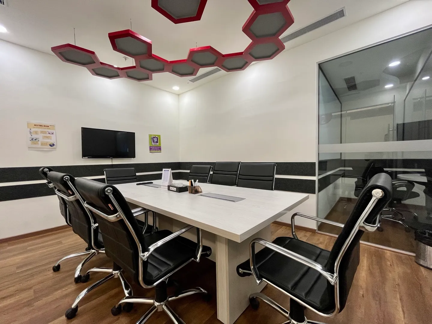 Six black leather chairs around a wood-grain table beneath red hexagon ceiling panels — AIHP managed office, Gurgaon
