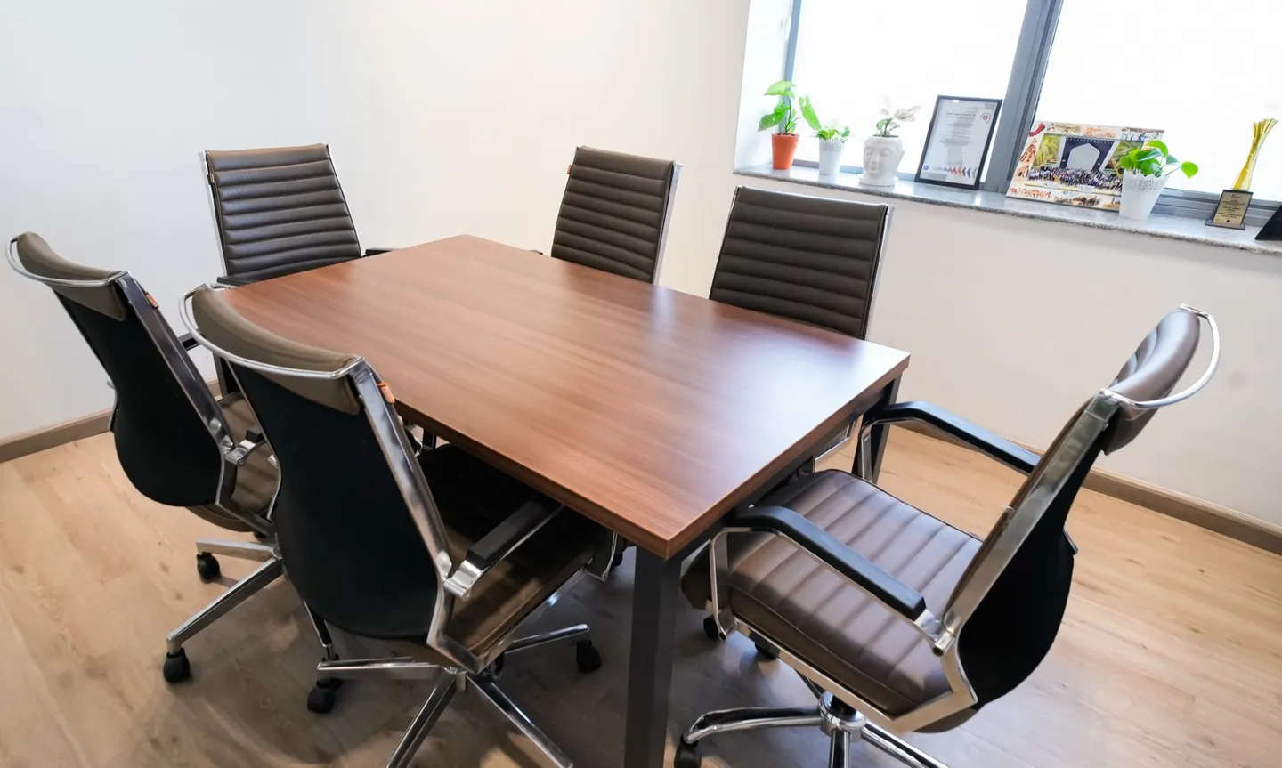 Six-seat walnut table with brown ribbed chairs and a window ledge of plants and trophies — AIHP managed office, Gurgaon