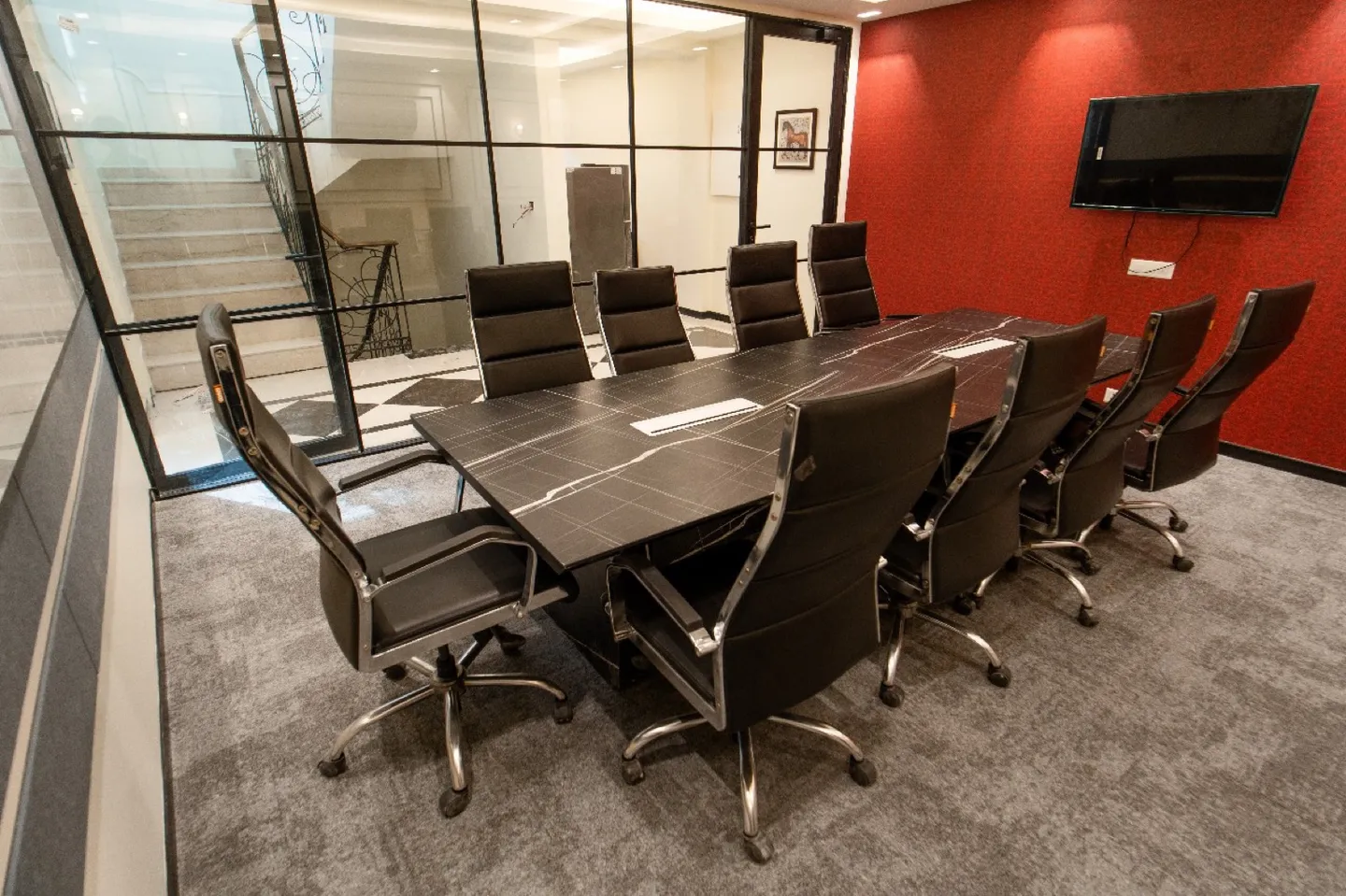Ten black leather chairs at a dark patterned table by a glass wall and red accent wall — AIHP managed office, Gurgaon