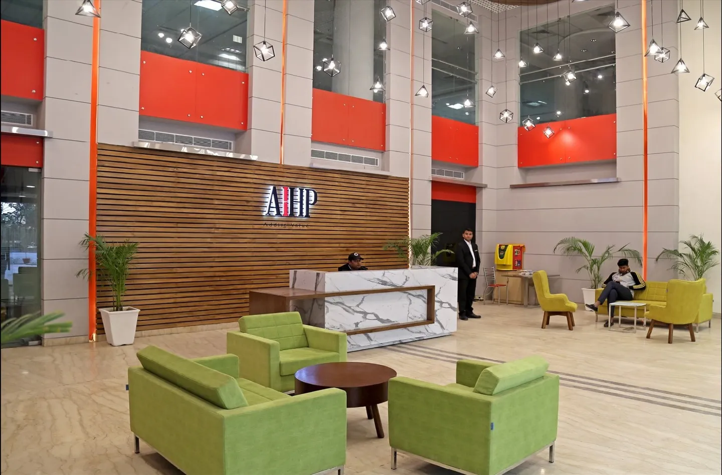 Atrium lobby with marble desk, AIHP wood feature wall and lime-green lounge chairs — AIHP managed office, Gurgaon