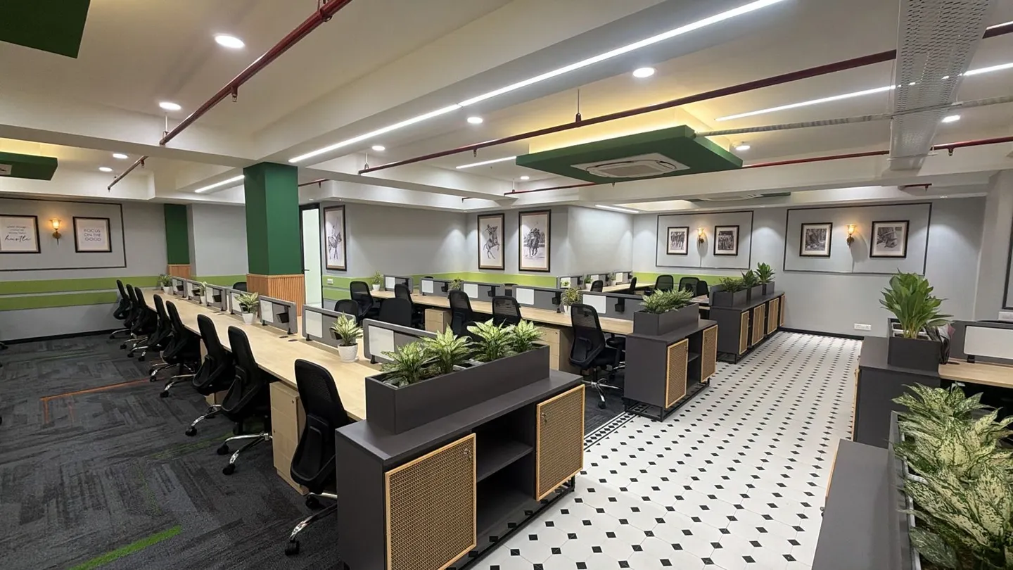 Wooden workstation rows with planters under green-accent walls and framed art — AIHP managed office, Gurgaon