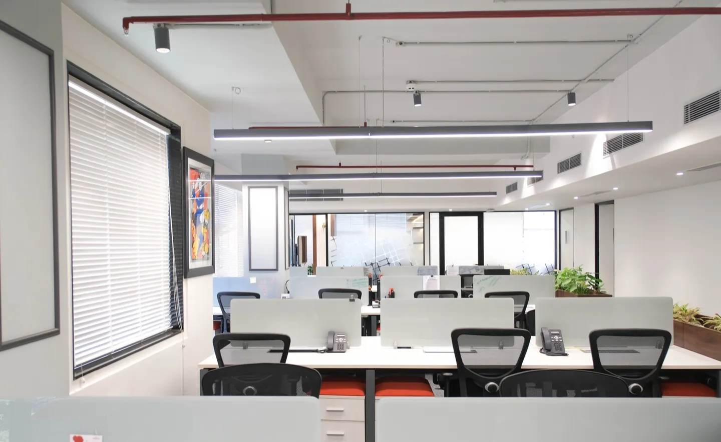 Desk pods with glass screens and phones, blinds, planters and framed art — AIHP managed office, Gurgaon