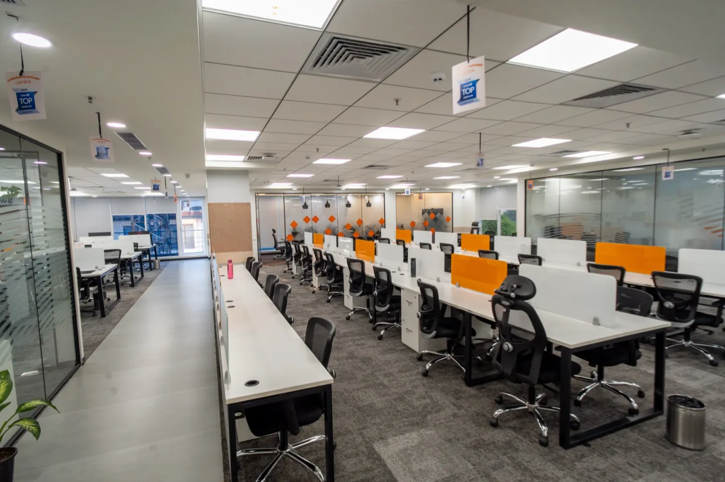 White desk rows with orange dividers, mesh chairs and glass cabins — AIHP managed office, Gurgaon