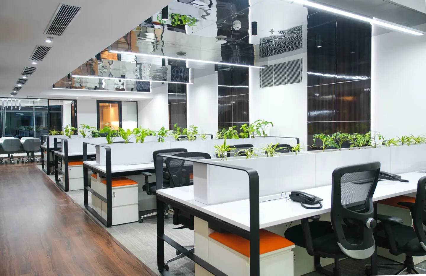 White workstations with orange seats, planters and glossy black ceiling panel — AIHP managed office, Gurgaon