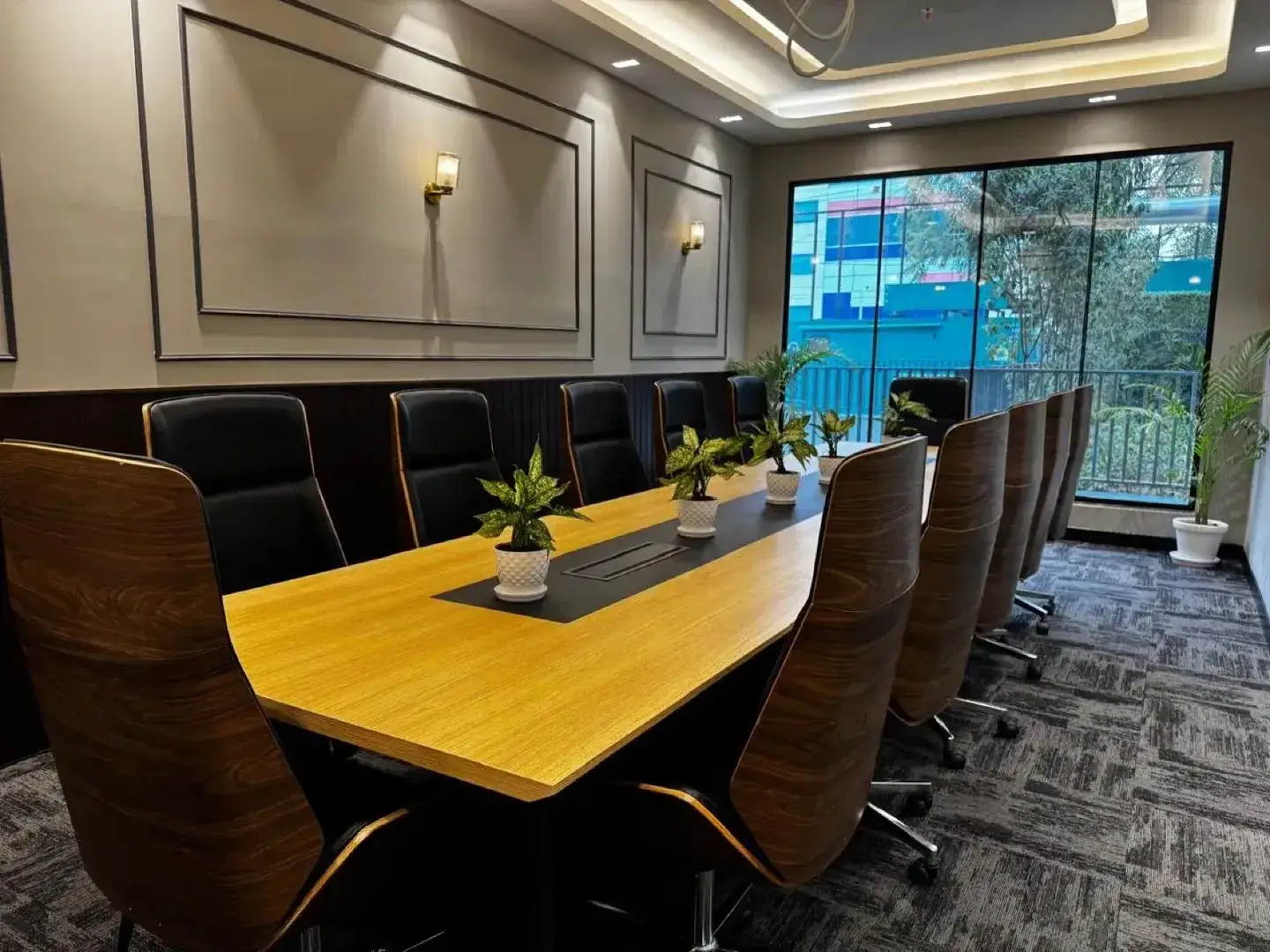 Ten-seat wood table with wood-back leather chairs and planters by a large window — AIHP managed office, Gurgaon