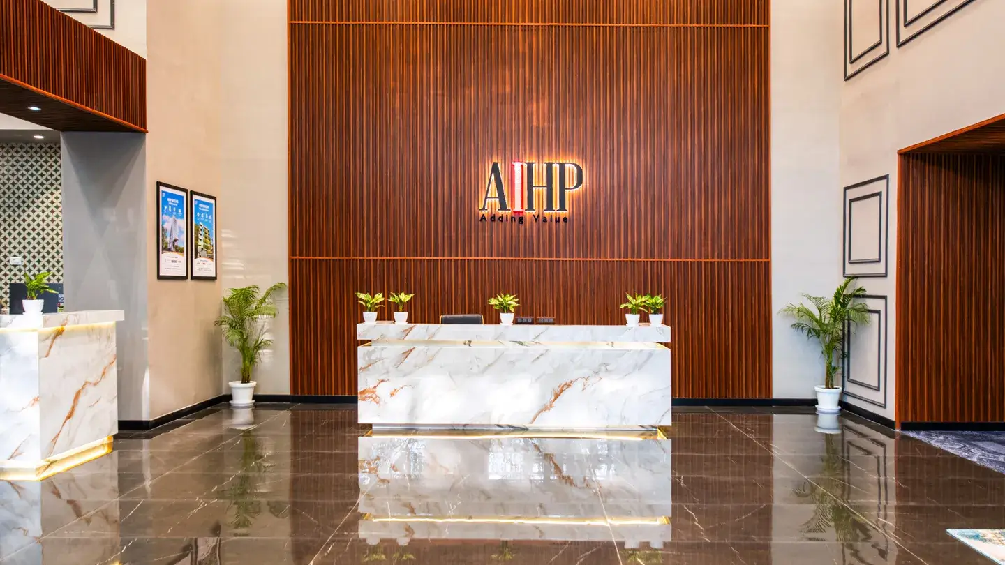 Backlit AIHP logo on a fluted walnut-slat wall above a white marble reception desk with brass underlighting — AIHP Millennium managed office lobby, Gurgaon